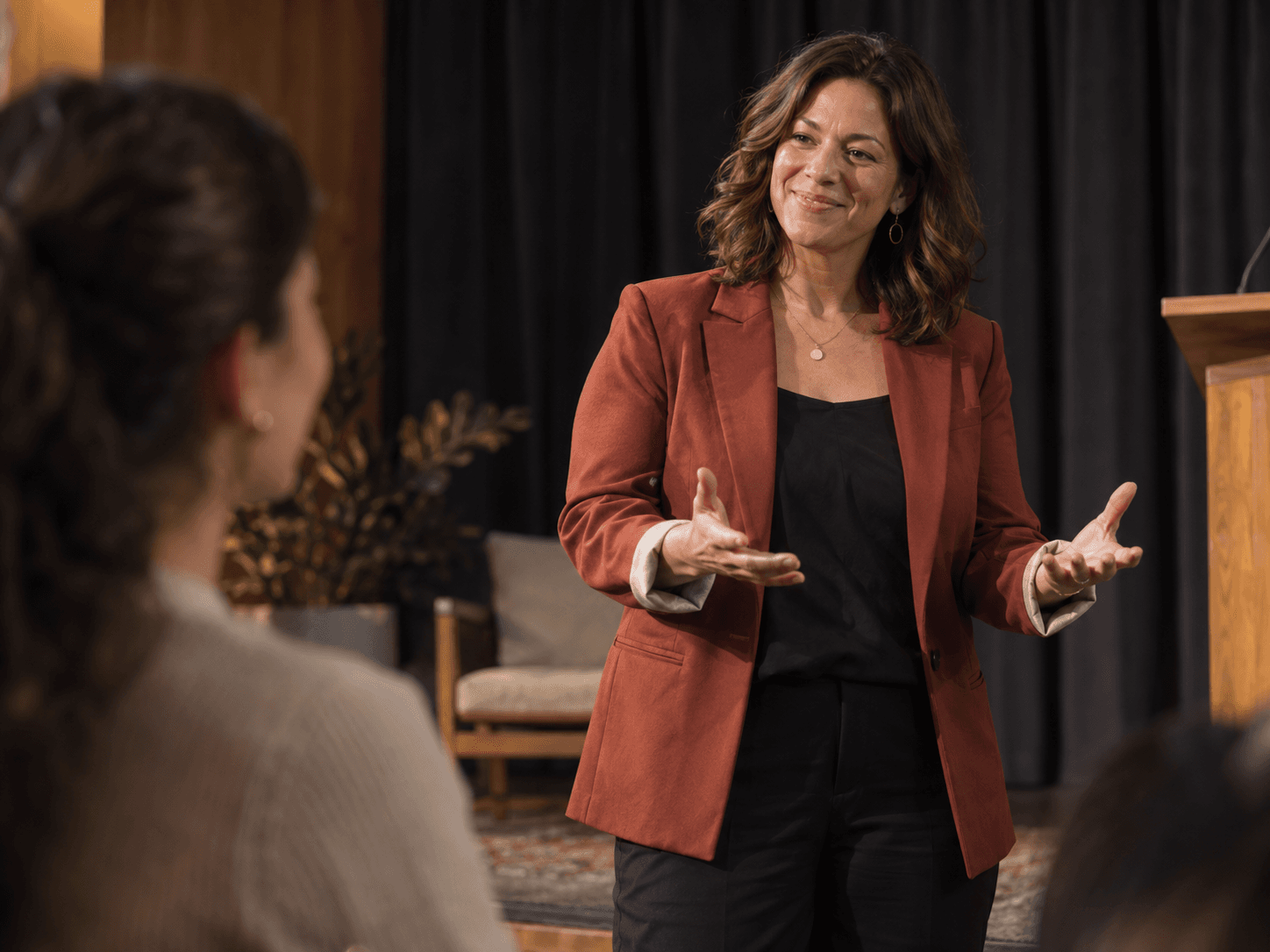 A woman in a brick-red blazer encouraging a participant during a community discussion